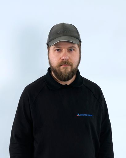 Bild von einem Mann mit Bart und einer Kappe. Er trägt einen schwarzen Pullover mit der Aufschrift „Orgami Sistec“ + Logo. Er steht vor einem weißen Hintergrund.