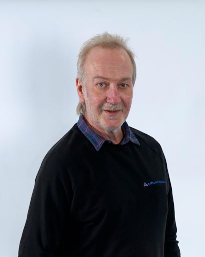 Bild von einem Mann mit Bart. Er trägt einen schwarzen Pullover mit der Aufschrift „Orgami Sistec“ und dem dazugehörigen Logo. Darunter trägt er ein kariertes Hemd. Er steht vor einem weißen Hintergrund.