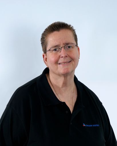 Bild von einer Frau mit kurzen Haaren und einer Brille. Sie trägt trägt ein schwarzes T-Shirt mit der Aufschrift „Orgami Sistec“ + Logo. Stehend vor einem weißen Hintergrund.