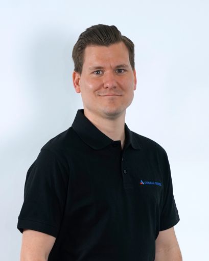 Bild von einem Mann mit braunen Haaren. Er trägt ein schwarzes T-Shirt mit der Aufschrift „Orgami Sistec“ + Logo. Stehend vor einem weißen Hintergrund.