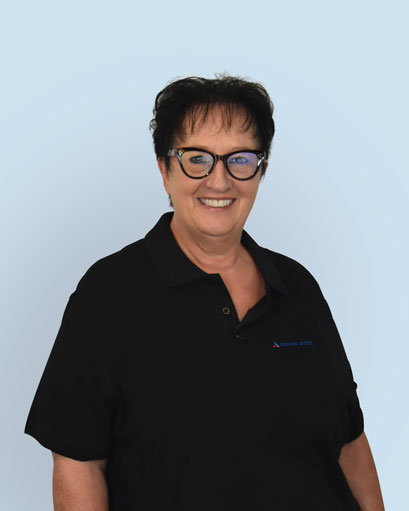 Bild von einer Frau mit kurzen Haaren und einer Brille. Sie trägt trägt ein schwarzes T-Shirt mit der Aufschrift „Orgami Sistec“ + Logo. Stehend vor einem weißen Hintergrund.