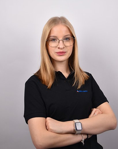 Bild von einer Frau mit offenen, blonden Haaren. Sie trägt eine Brille und ein schwarzes T-Shirt mit der Aufschrift „Orgami Sistec“ + Logo. Stehend vor einem weißen Hintergrund.