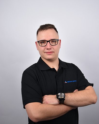 Bild von einem Mann mit Brille und braunen Haaren. Er trägt ein schwarzes T-Shirt mit der Aufschrift „Orgami Sistec“ + Logo. Stehend vor einem weißen Hintergrund.