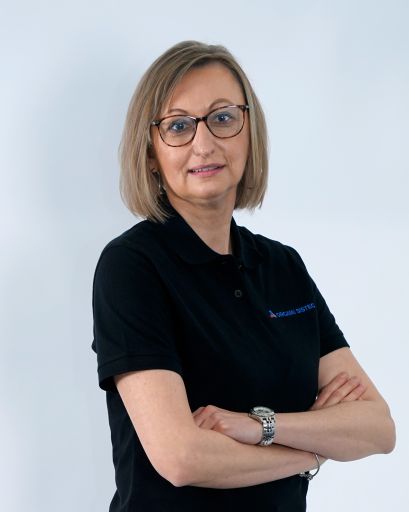 Bild von einer Frau mit blonden Haaren und einer Brille. Sie trägt trägt ein schwarzes T-Shirt mit der Aufschrift „Orgami Sistec“ + Logo. Stehend vor einem weißen Hintergrund.