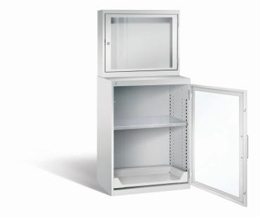 Lichtgrauer Computerschrank mit abschließbarem Sichtfenster im oberen Bereich und geöffneter Acrylglas-Stahltür im unteren Bereich und einem höhenverstellbarer Fachboden sowie Auszugsboden. Der Schrank steht vor weißem Hintergrund.