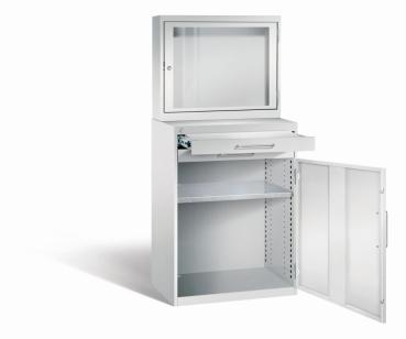 Lichtgrauer Computerschrank mit abschließbarem Sichtfenster im oberen Bereich und geöffneter Stahltür mit zwei Schubladen im unteren Bereich und einem höhenverstellbarer Fachboden. Der Schrank steht vor weißem Hintergrund.