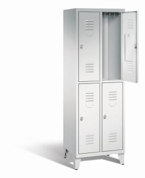 Ein lichtgrauer Garderobenschrank mit zwei Abteilen, vier Fächern sowie integrierten Kleiderstangen mit Kleiderhaken, dessen obere rechte Tür geöffnet ist. Er steht auf Stahlblechfüßen vor weißem Hintergrund.