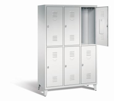 Ein lichtgrauer Garderobenschrank mit drei Abteilen, sechs Fächern sowie integrierten Kleiderstangen mit Kleiderhaken, dessen obere rechte Tür geöffnet ist. Er steht auf Stahlblechfüßen vor weißem Hintergrund.