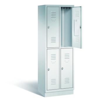 Ein lichtgrauer Garderobenschrank mit zwei Abteilen, vier Fächern sowie integrierten Kleiderstangen mit Kleiderhaken, dessen obere rechte Tür geöffnet ist. Er steht auf einem Stahlblechsockel vor weißem Hintergrund.