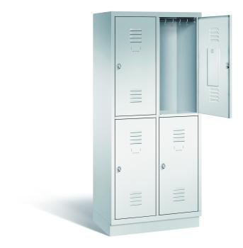 Ein lichtgrauer Garderobenschrank mit zwei Abteilen, vier Fächern sowie integrierten Kleiderstangen mit Kleiderhaken, dessen obere rechte Tür geöffnet ist. Er steht auf einem Stahlblechsockel vor weißem Hintergrund.