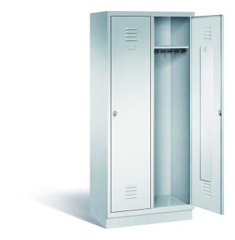 Ein lichtgrauer Garderobenschrank mit zwei Abteilen, zwei Fächern sowie integrierten Kleiderstangen mit Kleiderhaken, dessen rechte Tür geöffnet ist. Er steht auf einem Stahlblechsockel vor weißem Hintergrund.