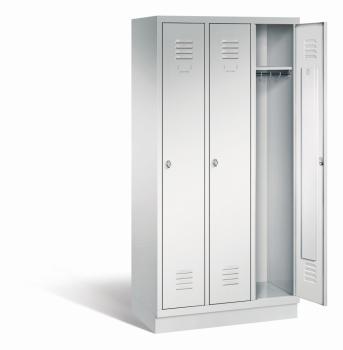 Ein lichtgrauer Garderobenschrank mit drei Abteilen, drei Fächern sowie integrierten Kleiderstangen mit Kleiderhaken, dessen rechte Tür geöffnet ist. Er steht auf einem Stahlblechsockel vor weißem Hintergrund.
