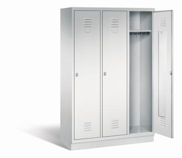 Ein lichtgrauer Garderobenschrank mit drei Abteilen, drei Fächern sowie integrierten Kleiderstangen mit Kleiderhaken, dessen rechte Tür geöffnet ist. Er steht auf einem Stahlblechsockel vor weißem Hintergrund.
