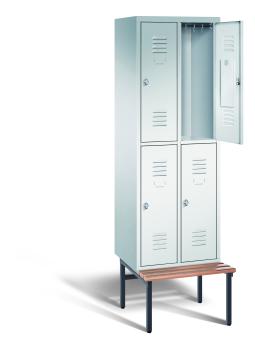 Ein lichtgrauer Garderobenschrank mit zwei Abteilen, vier Fächern sowie integrierten Kleiderstangen mit Kleiderhaken, dessen obere rechte Tür geöffnet ist. Er steht auf einer unter- und vorgebauten Sitzbank vor weißem Hintergrund.
