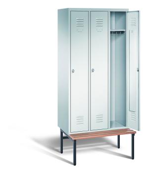Ein lichtgrauer Garderobenschrank mit drei Abteilen, drei Fächern sowie integrierten Kleiderstangen mit Kleiderhaken, dessen rechte Tür geöffnet ist. Er steht auf einer unter- und vorgebauten Sitzbank vor weißem Hintergrund.
