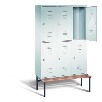 Ein lichtgrauer Garderobenschrank mit drei Abteilen, sechs Fächern sowie integrierten Kleiderstangen mit Kleiderhaken, dessen obere rechte Tür geöffnet ist. Er steht auf einer unter- und vorgebauten Sitzbank vor weißem Hintergrund.