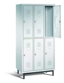 Ein lichtgrauer Garderobenschrank mit drei Abteilen, sechs Fächern sowie integrierten Kleiderstangen mit Kleiderhaken, dessen obere rechte Tür geöffnet ist. Er steht auf Stahlrohrfüßen vor weißem Hintergrund.