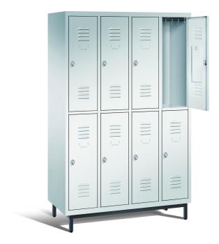 Ein lichtgrauer Garderobenschrank mit vier Abteilen, acht Fächern sowie integrierten Kleiderstangen mit Kleiderhaken, dessen obere rechte Tür geöffnet ist. Er steht auf Stahlrohrfüßen vor weißem Hintergrund.