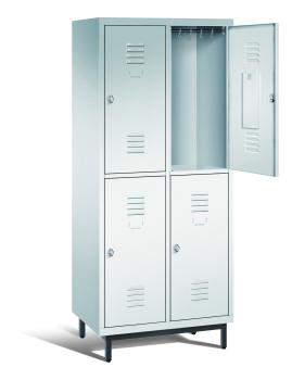 Ein lichtgrauer Garderobenschrank mit zwei Abteilen, vier Fächern sowie integrierten Kleiderstangen mit Kleiderhaken, dessen obere rechte Tür geöffnet ist. Er steht auf Stahlrohrfüßen vor weißem Hintergrund.