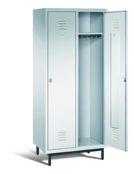 Ein lichtgrauer Garderobenschrank mit zwei Abteilen, zwei Fächern sowie integrierten Kleiderstangen mit Kleiderhaken, dessen rechte Tür geöffnet ist. Er steht auf Stahlrohrfüßen vor weißem Hintergrund.