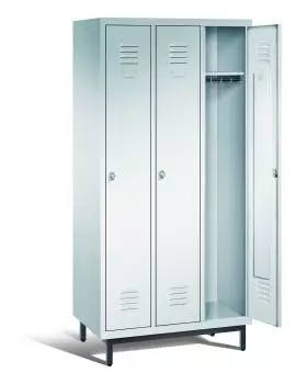 Ein lichtgrauer Garderobenschrank mit drei Abteilen, drei Fächern sowie integrierten Kleiderstangen mit Kleiderhaken, dessen rechte Tür geöffnet ist. Er steht auf Stahlrohrfüßen vor weißem Hintergrund.
