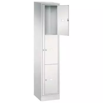 Lichtgrauer Wäschetauschrank vor weißem Hintergrund mit Drehriegel. Der Schrank besitzt 3 Fächer, wovon das erste geöffnet ist. Unterhalb befindet sich ein Stahlblechsockel.