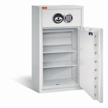 Ein lichtgrauer Deposittresor dessen Tür geöffnet ist. Im Türinnenraum befinden sich eine sichtbare Türverriegelung und ein Zertifikat. Der Innenraum ist leer und verfügt über zwei Fachböden. Der Tresor steht vor einem weißen Hintergrund