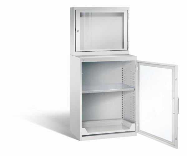 Lichtgrauer Computerschrank mit abschließbarem Sichtfenster im oberen Bereich und geöffneter Acrylglas-Stahltür im unteren Bereich und einem höhenverstellbarer Fachboden sowie Auszugsboden. Der Schrank steht vor weißem Hintergrund.