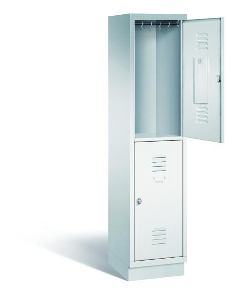 Ein lichtgrauer Garderobenschrank mit einem Abteil, zwei Fächern sowie integrierten Kleiderstangen mit Kleiderhaken, dessen obere Tür geöffnet ist. Er steht auf einem Stahlblechsockel vor weißem Hintergrund.