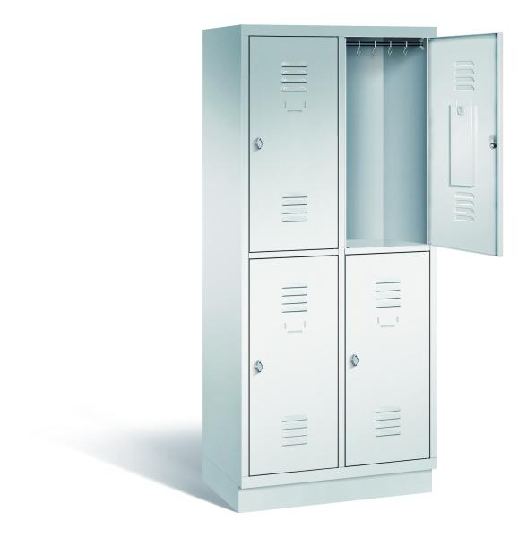Ein lichtgrauer Garderobenschrank mit zwei Abteilen, vier Fächern sowie integrierten Kleiderstangen mit Kleiderhaken, dessen obere rechte Tür geöffnet ist. Er steht auf einem Stahlblechsockel vor weißem Hintergrund.