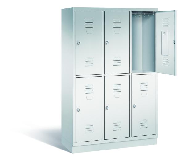 Ein lichtgrauer Garderobenschrank mit drei Abteilen, sechs Fächern sowie integrierten Kleiderstangen mit Kleiderhaken, dessen obere rechte Tür geöffnet ist. Er steht auf einem Stahlblechsockel vor weißem Hintergrund.