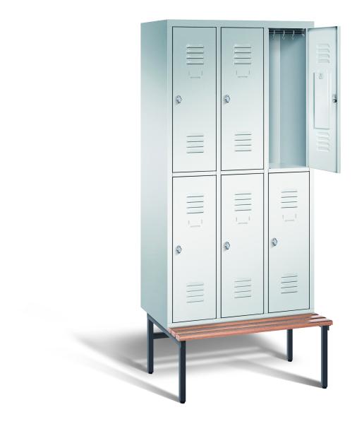 Ein lichtgrauer Garderobenschrank mit drei Abteilen, sechs Fächern sowie integrierten Kleiderstangen mit Kleiderhaken, dessen obere rechte Tür geöffnet ist. Er steht auf einer unter- und vorgebauten Sitzbank vor weißem Hintergrund.
