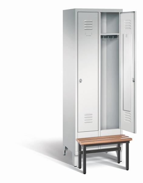 Ein lichtgrauer Garderobenschrank mit zwei Abteilen, zwei Fächern sowie integrierten Kleiderstangen mit Kleiderhaken, dessen rechte Tür geöffnet ist. Er steht auf Stahlblechfüßen und hat eine vorgebaute Sitzbank vor weißem Hintergrund.
