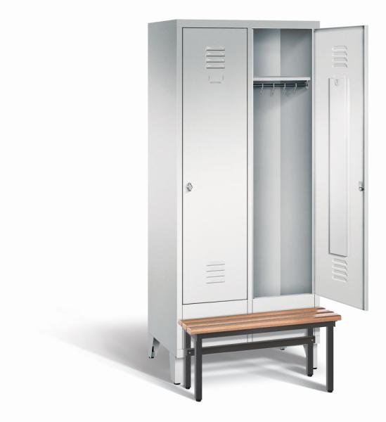 Ein lichtgrauer Garderobenschrank mit zwei Abteilen, zwei Fächern sowie integrierten Kleiderstangen mit Kleiderhaken, dessen rechte Tür geöffnet ist. Er steht auf Stahlblechfüßen und hat eine vorgebaute Sitzbank vor weißem Hintergrund.