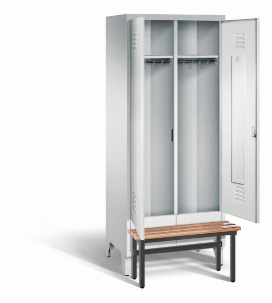 Ein lichtgrauer Garderobenschrank mit zwei Abteilen, zwei Fächern sowie integrierten Kleiderstangen mit Kleiderhaken, dessen Türen geöffnet sind. Er steht auf Stahlblechfüßen und hat eine vorgebaute Sitzbank vor weißem Hintergrund.