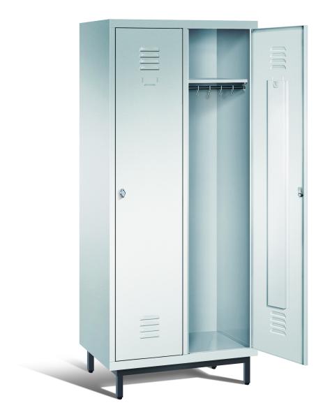Ein lichtgrauer Garderobenschrank mit zwei Abteilen, zwei Fächern sowie integrierten Kleiderstangen mit Kleiderhaken, dessen rechte Tür geöffnet ist. Er steht auf Stahlrohrfüßen vor weißem Hintergrund.